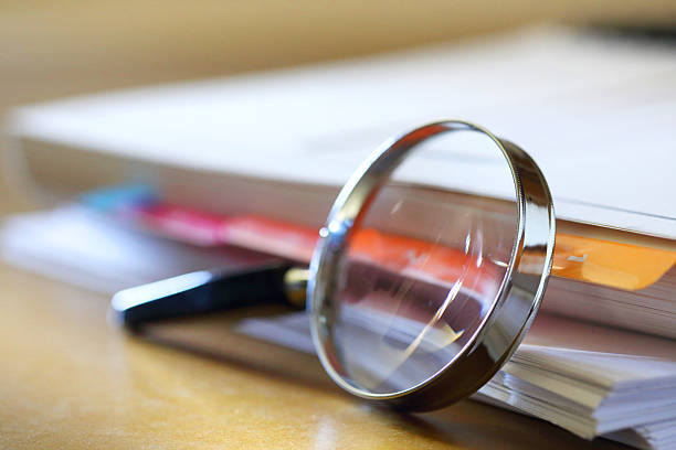 istock Magnifying Glass Leaning Against Stack Of Papers 2219949221