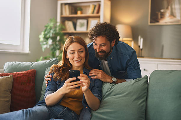 istock Happy couple relaxing on sofa and browsing smartphone at home 2219950113