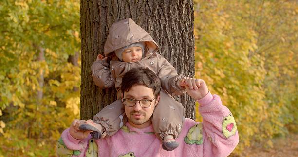 In a beautiful and vibrant forest setting adorned with colorful autumn foliage, a person joyfully carries a child on their shoulders, capturing a playful and unforgettable moment in nature