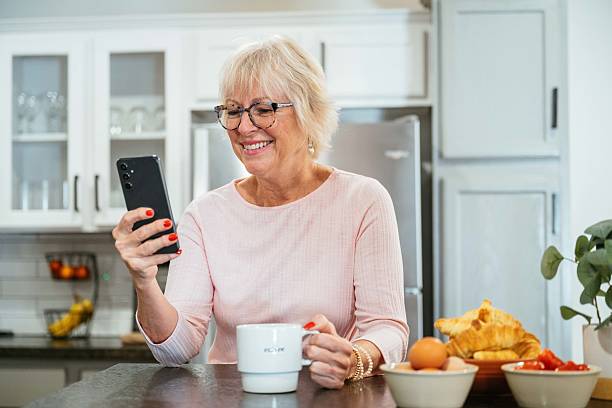 istock Elderly woman in a light kitchen enjoys coffee while using her smartphone with a smile on her face 2219960830