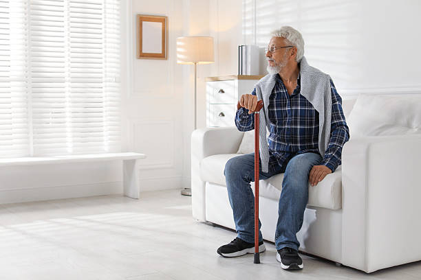 istock Lonely senior man with walking cane sitting on sofa at home. Space for text 2219961003