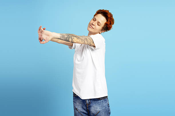 istock Young woman with tattoos stretching arms on blue background 2219963097