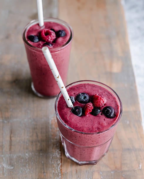 Two glasses of thick berry smoothie topped with frozen berries and served with paper straws