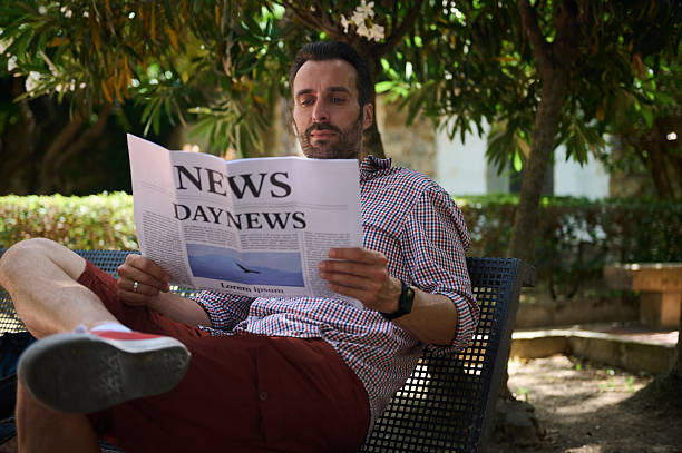 Full length shot of a young man in pyjamas standing and reading a newspaper isolated on white background