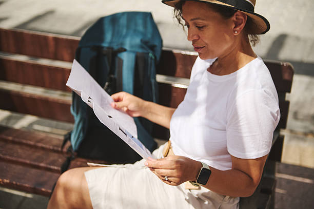 istock A woman sitting on a bench in a bright urban setting reads a map, exploring her surroundings. 2219969701