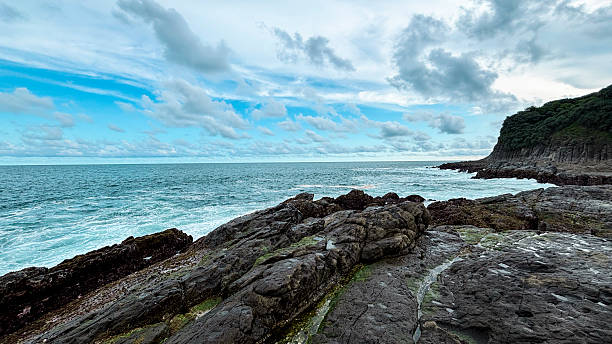 istock Rocky Seaside Cliff with Crashing Waves Under Cloudy Sky 2219973195