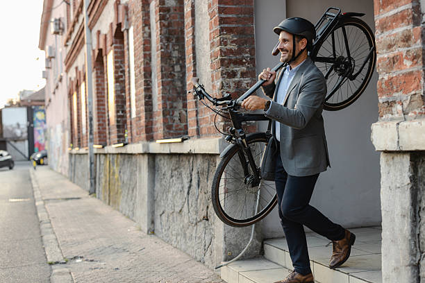 istock Businessman carrying bicycle outdoors in urban setting on his way to work 2219975033