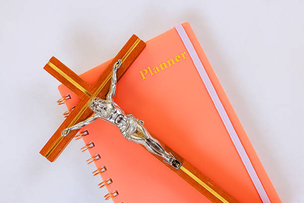 Silver crucifix rests on top of coral planner with metallic spiral binding an elastic band across cover.