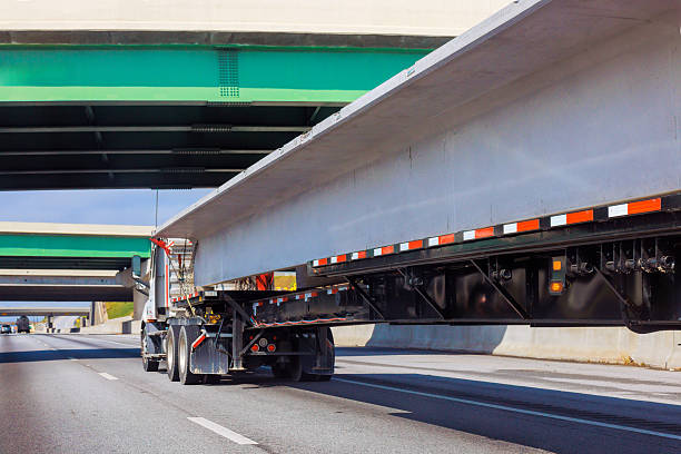 istock Truck transporting long concrete slabs on busy highway under overpasses during day 2219984260