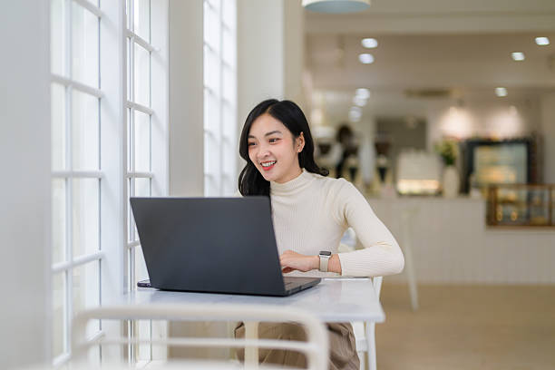 istock Young professional typing on laptop, experiencing modern remote workspace in sunlit coffee shop 2219988564