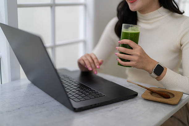 Young businesswoman using her laptop while enjoying a healthy green juice, promoting a balanced work-life