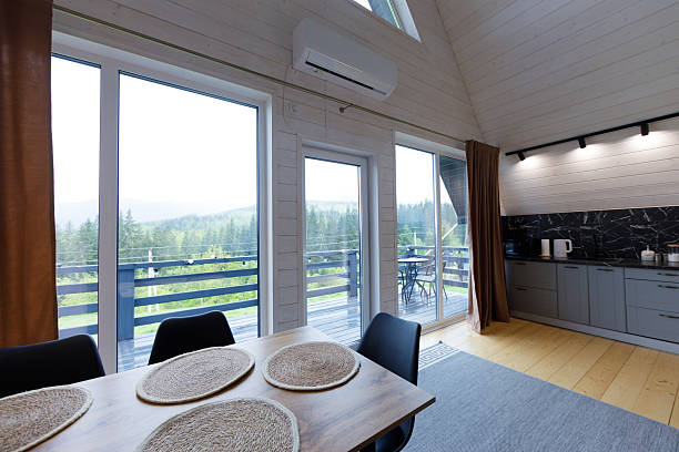 istock Modern and Cozy Interior of a Rustic Cabin Featuring Large Windows Overlooking Lush Green Forested Hills and a Simple Yet Elegant Dining Area with Natural Decor Elements 2219988825