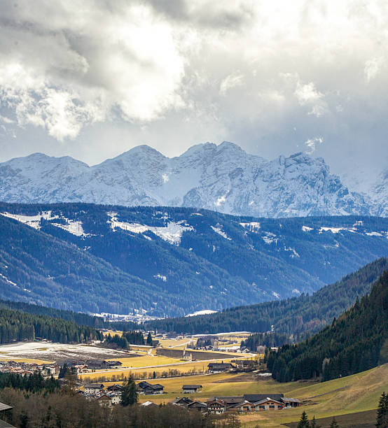 Traditional village in valley below snowcapped mountains, Dolomites