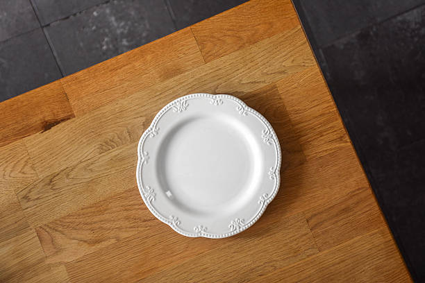 Overhead shot of an elegant white porcelain plate with delicate detailing, set on a warm wood surface with slate-style tiles in the background.
