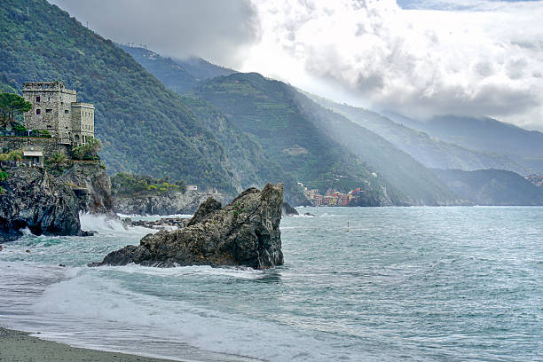 Rugged coastline, beach, sea and village with sun rays shining on water, Cinque Terre