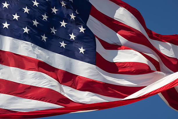 istock American Flag Waving In The Wind Against Deep Blue Sky. 2219993488