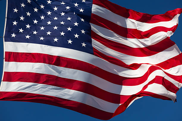 istock American Flag Waving In The Wind Against Deep Blue Sky. 2219993506