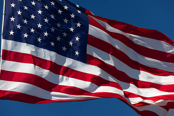 istock American Flag Waving In The Wind Against Deep Blue Sky. 2219993515
