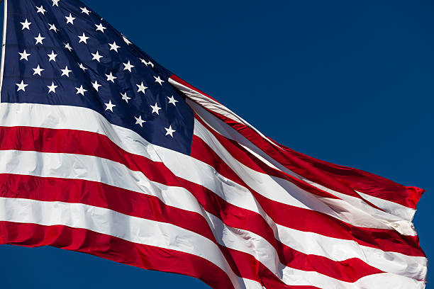 istock American Flag Waving In The Wind Against Deep Blue Sky. 2219993523