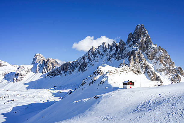 Mountain hut on mountain pass below snowcapped peaks, sunny day, Dolomites