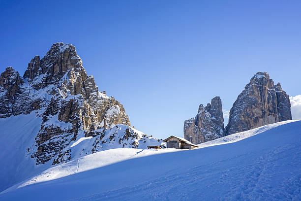 Mountain hut on mountain pass below snowcapped peaks, sunny day, Dolomites