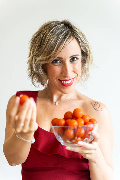 Smiling woman holding bowl of cherry tomatoes and showing one