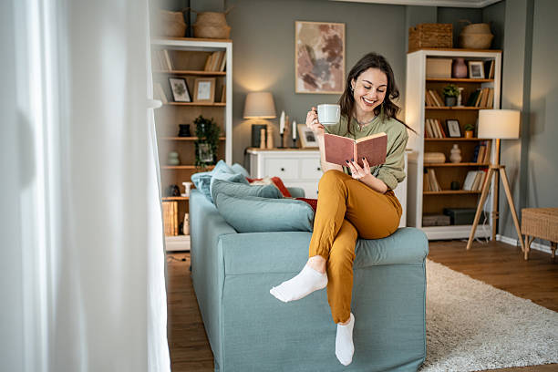 istock Young woman reading a book and drinking tea on sofa at home 2219997650