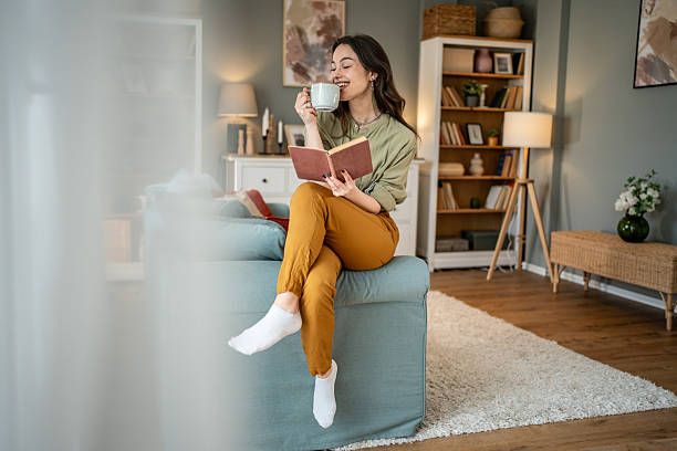 istock Young woman relaxing on sofa, reading a book and drinking tea 2219997717
