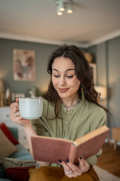 istock Young woman reading a book and drinking tea at home 2219998976