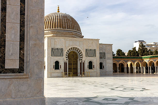 istock A building with a dome and arched openings is featured in a spacious, light-colored courtyard. 2219999891