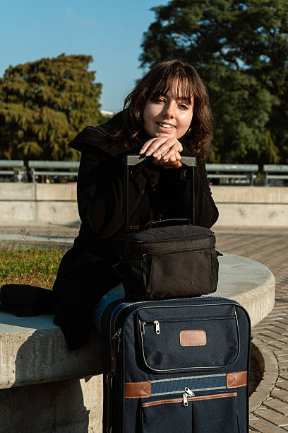 istock Woman waiting with suitcase on park bench 2220000459