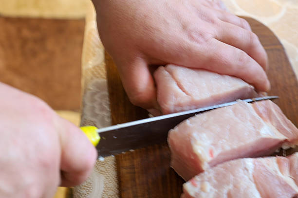 istock Hands are cutting fresh meat on a wooden board, reflecting the preparation process for cooking. This shot focuses on culinary actions and ingredients for a future dish. 2220003738