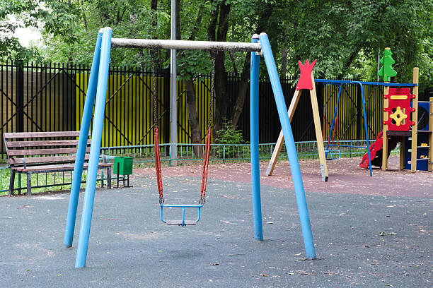 istock Blue swing set with a red seat is in a park. There is a bench nearby. The park is empty 2220004557