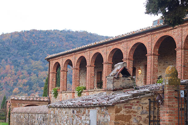Trequanda, Italy: Historic Tuscan architecture featuring a brick colonnade with stone details, part of a charming castle hotel, set against a scenic hillside backdrop.