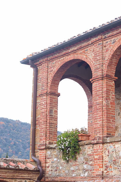 Trequanda, Italy: Historic Tuscan architecture featuring a brick colonnade with stone details, part of a charming castle hotel, set against a scenic hillside backdrop.