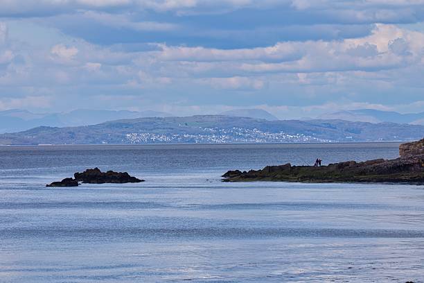 istock A serene seascape features a rocky outcrop and a coastal structure under a soft, clouded sky. 2220005980