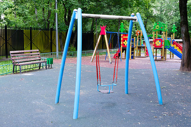 istock Blue swing set with a red seat is in a park. There is a bench nearby. The park is empty 2220009485