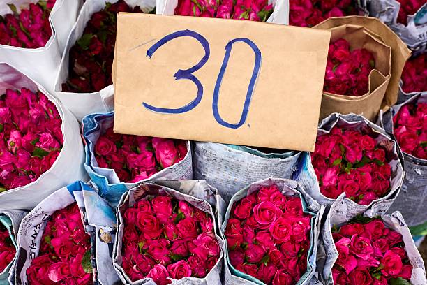Tightly bundled pink roses are wrapped in newspaper and set beneath a cardboard sign.