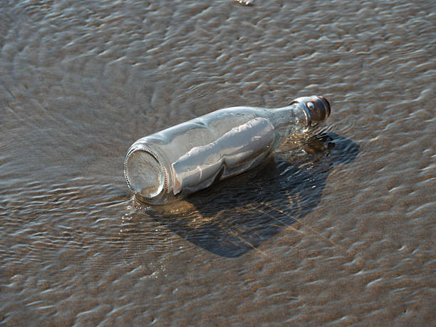 A worn glass bottle rests on a sandy beach with waves lapping the shore, evoking thoughts of messages or journeys. The scene suggests tranquility and mystery.