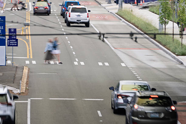 Pedestrians cross a busy street on a crosswalk in Seattle Washington.  Cars wait at the light.