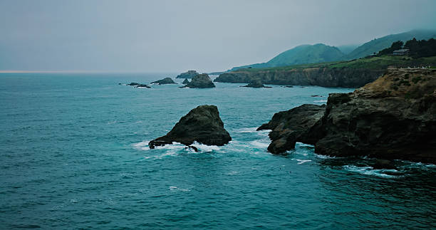 Aerial shot of craggy coastline in fog at dusk in Mendocino County on the Northern California coast near Fort Bragg.