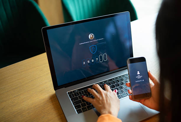 Asian woman authorizing her identity by entering code from her phone to log in to her laptop.
