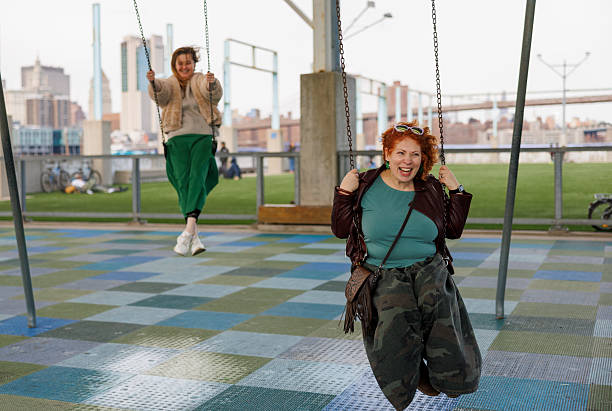 istock Swinging adults enjoy playground fun. Brooklyn park with Manhattan skyline backdrop. 2220036678