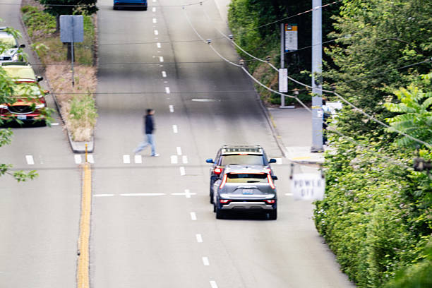 Pedestrian cross a busy street on a crosswalk in Seattle Washington.  Cars wait at the light.