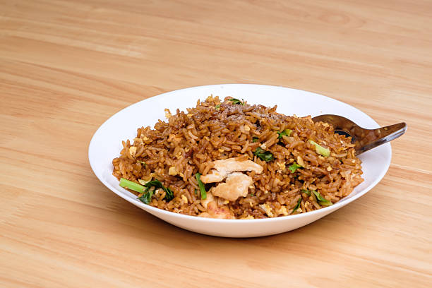 istock Thai style dark brown soy sauce fried rice with chicken, kale, and egg in white dish with short spoon on light wooden table 2220045294