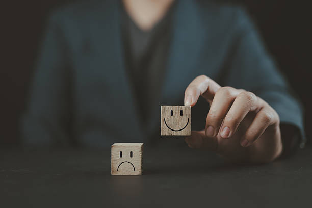 istock Customer service review. Client holds a smiley happy face on wooden cube with text review symbol. Feedback rating, Think positive, satisfaction survey. World Mental Health Day. Pleasure and Sadness. 2220047829