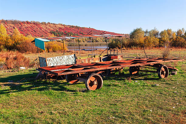 Abandoned metal transport sits on a grassy field beside a river. Weathered transport vehicle, its frame showing the passage of time, stands in a rural setting
