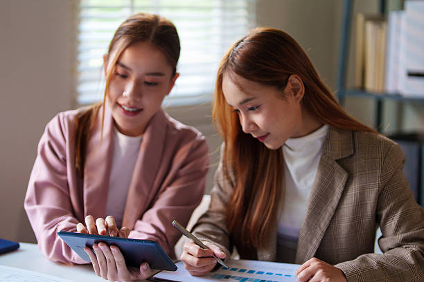 istock Two businesswomen sit together in an office setting, with one showing something on her smartphone to the other. They are engaged and focused. 2220055159