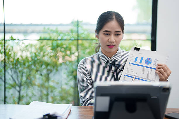 istock young woman is sitting at her desk, holding a document and explaining something during a video call on her tablet. She is smiling and engaged in the conversation, 2220055590