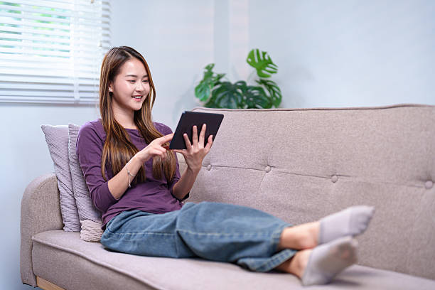 istock A young woman sitting on a sofa, using a tablet with a smile, enjoying her leisure time at home 2220056622
